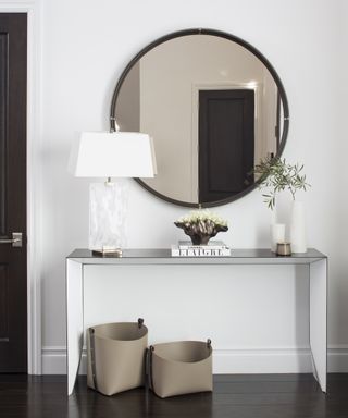 A modern hallway idea with a black and white console table and round mirror with brown tinted glass
