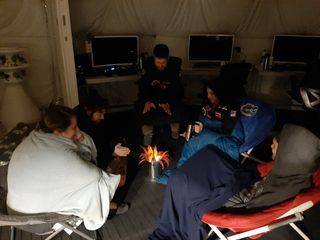 All crewmembers huddle to share their personal life stories around a "campfire" at HI-SEAS (consisting of electronic candles and a paper plant in a metallic can).