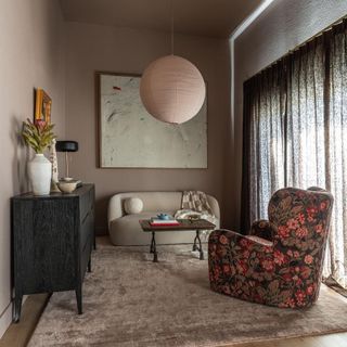 A living room with a rice paper lantern, a beige couch, a patterned sofa seater and wall art