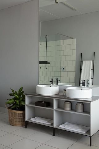 Tiled bathroom with his and hers washbasins. A basket with a green plant is next to it.