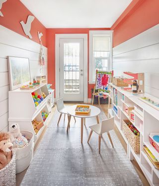 A narrow playroom with orange walls and white cubbies