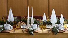 Christmas table setting on bare wooden table with glass trees, greenery, candles and coloured yellow glasses 