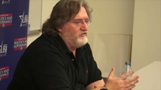 Gabe Newell in black shirt sitting at white desk for 2013 university talk