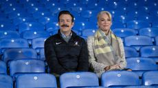 Ted Lasso (Jason Sudeikis) and Rebecca Welton (Hannah Waddingham) sitting in the stands in "Ted Lasso" season 3