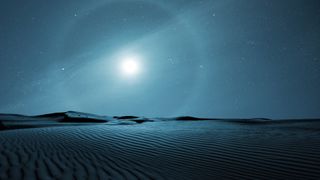 moon halo in the sky above sweeping desert sand dunes. 