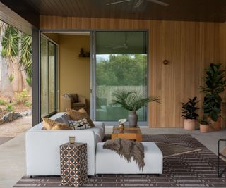 white garden sofa under a wood clad covering with rug and accessories in a neutral palette