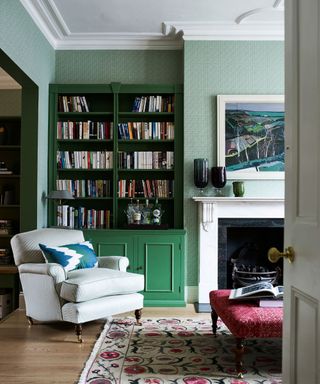 green wallpapered living room with dark green painted bookshelves and an opening to the adjoining room also in a green scheme