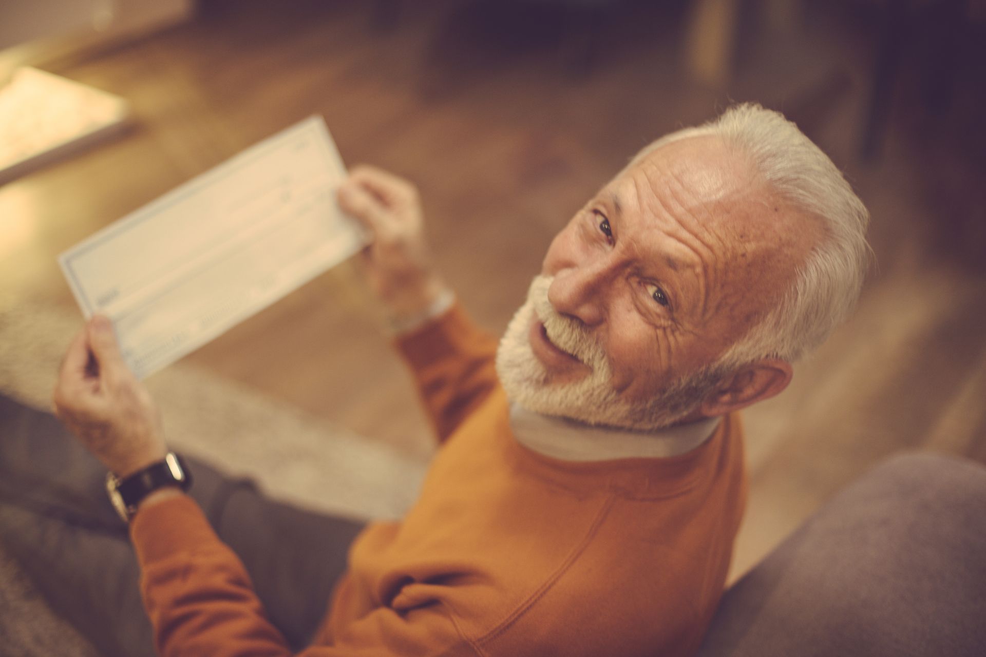 Retirement days have begun. Senior man holding bank check. Close up. Looking at camera.
