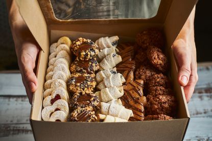 A person holds a box filled with sweet treats.