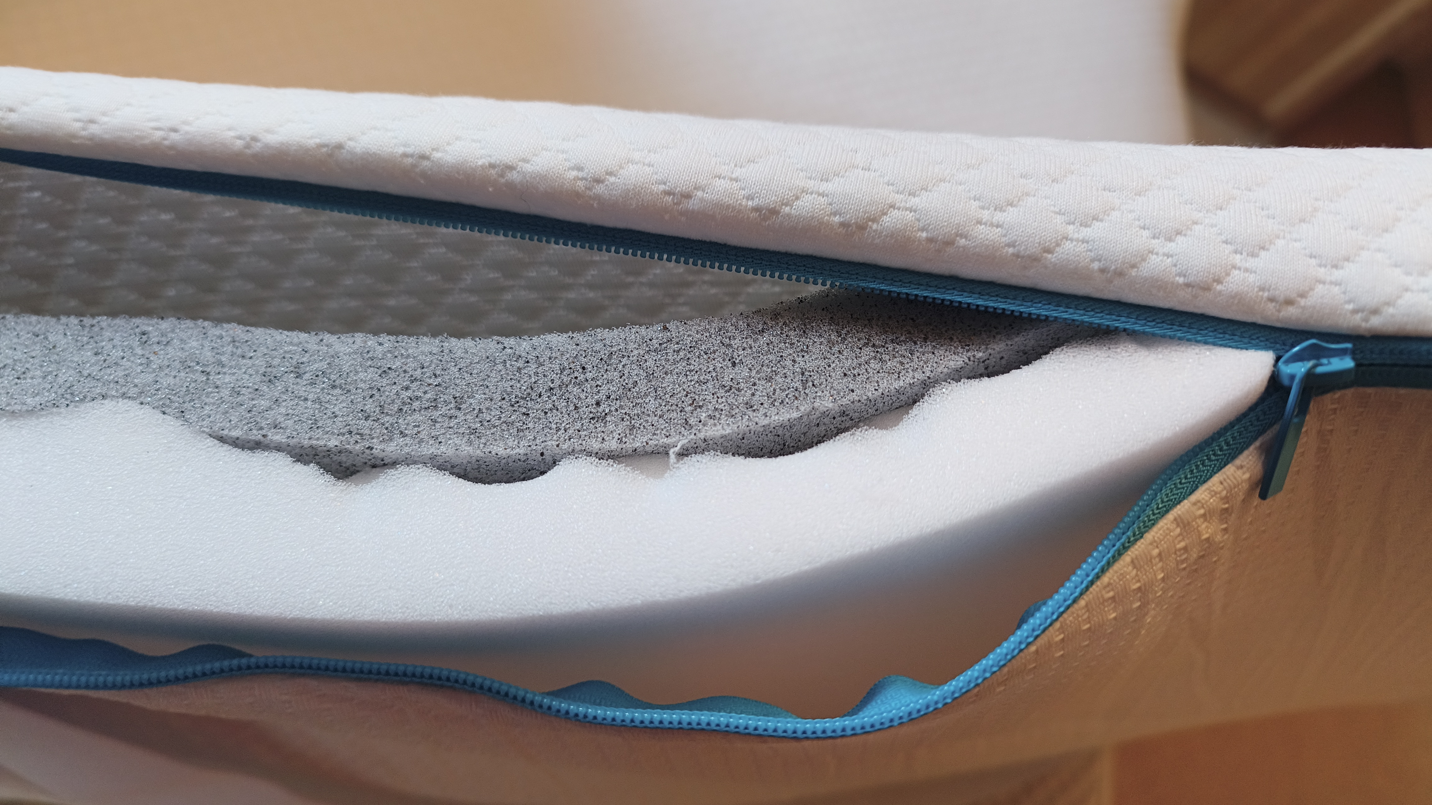 The removable cover of the Simba Cool Foam Mattress Topper unzipped at the edge, revealing the dark graphite-infused Simbatex foam layer above the white contoured foam base.