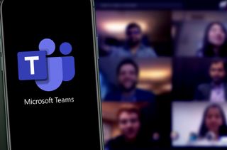 The Microsoft Teams logo on a smartphone in front of a Teams meeting