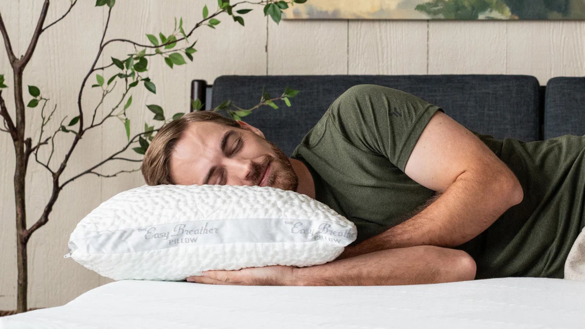 A man wearing a green t shirt lying on his side with his head resting on the Nest Bedding Easy Breather Side Sleeper Pillow