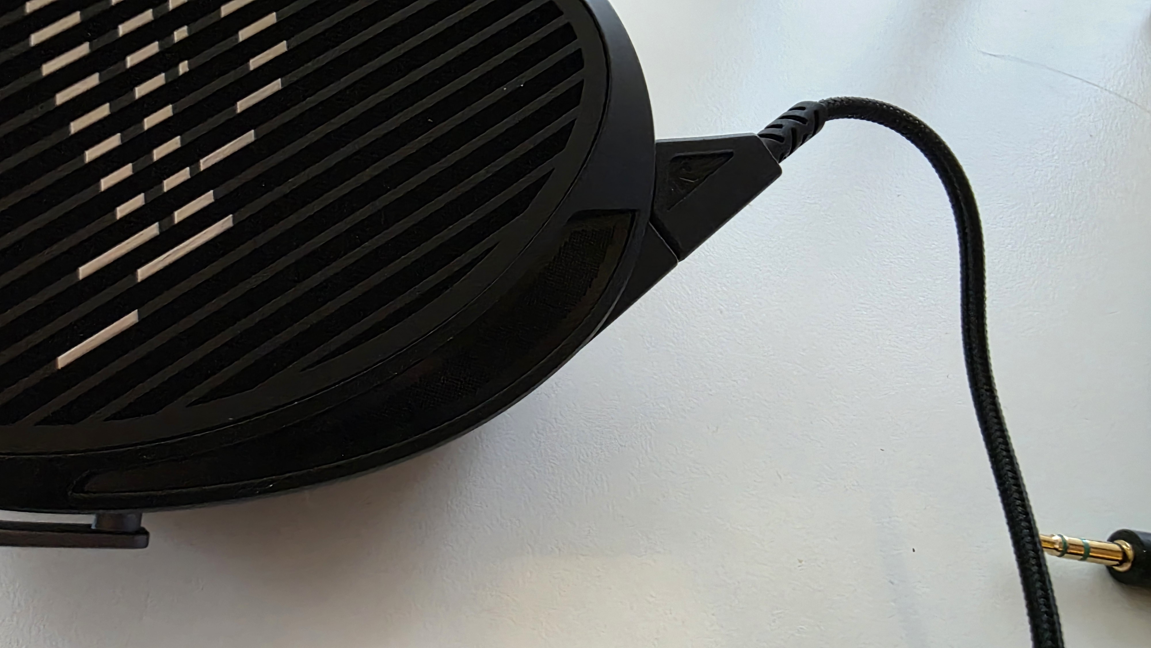 Close-up of a black headphone with a ribbed design on the ear cup, connected by a braided audio cable. It rests on a white surface.