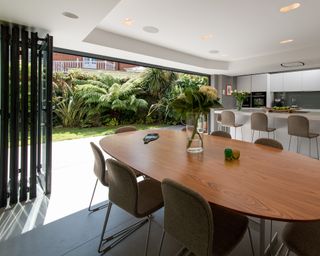 A large modern kitchen with island, bar stools, large round dining table and bi-fold doors - one of four window glazing options provided by IDSystems
