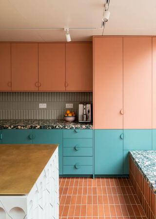 Blue lower cabinets and contrasting pink upper cabinets in a modern kitchen. An island sits in the middle of a kitchen and contrasting tiles have been placed for the flooring.