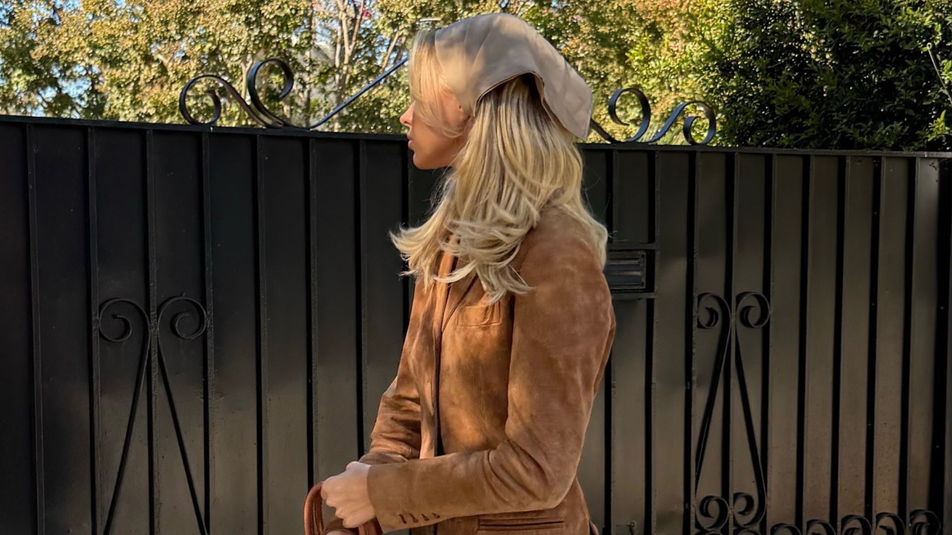 Model Elsa Hosk poses for a photo outside wearing a brown suede jacket with brown loafers, a brown Hermes bag and light-wash blue jeans.