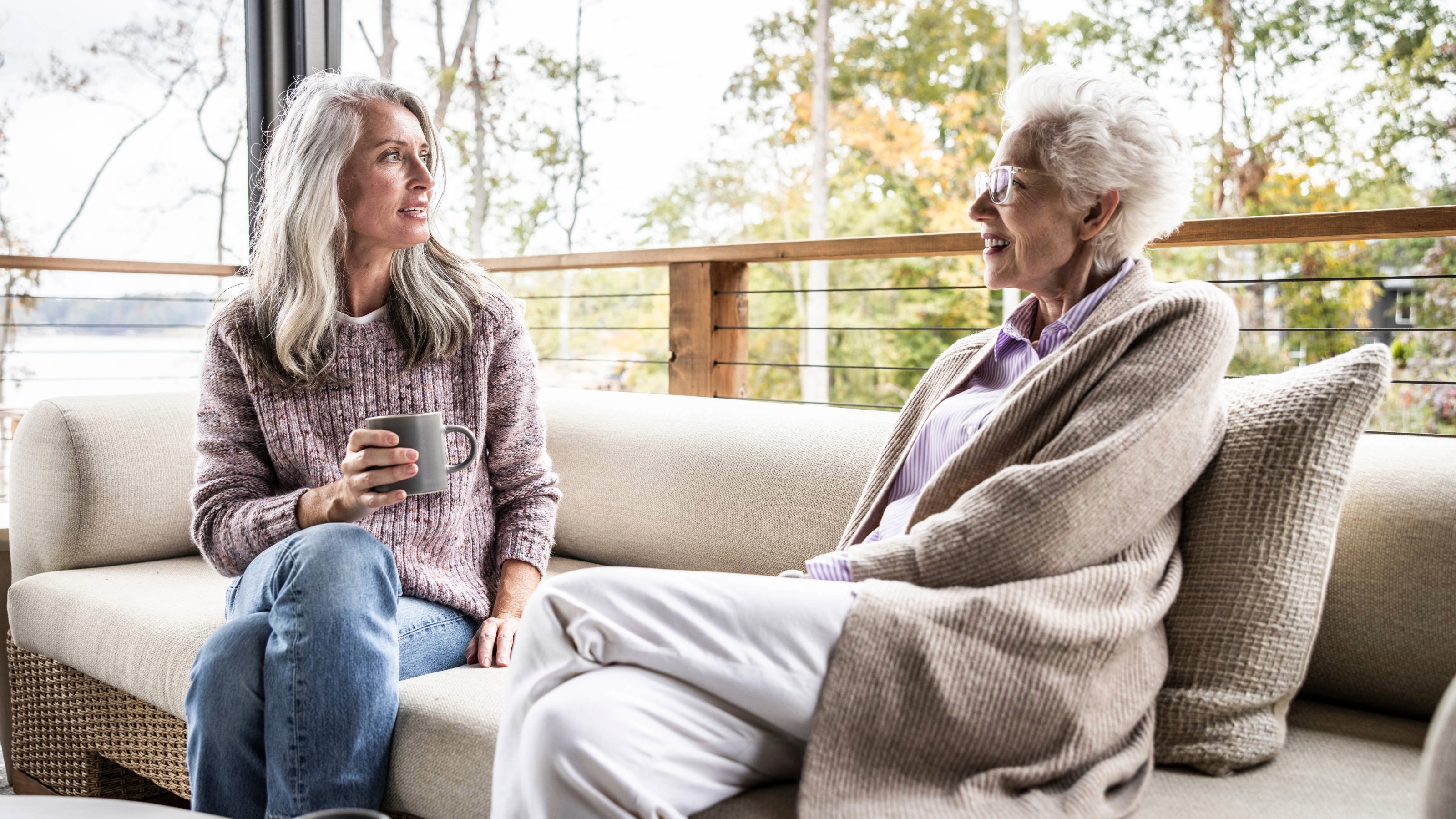 Senior mother and daughter having coffee and talking on back porch 