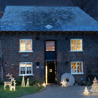 house dresed with warm white lights on exterior with illumianted trees stars and reindeers