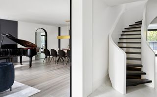 Hallway with white curved staircase and entrance to room with black piano in