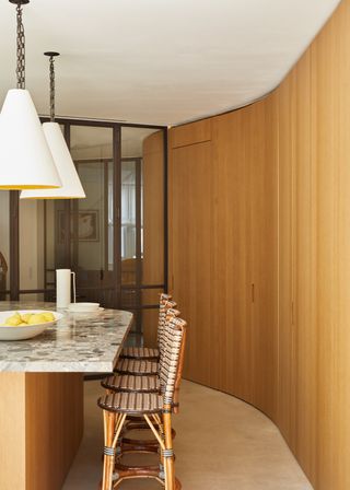 a curved wall in a kitchen and an island with a countertop overhang. Beside the kitchen island are bar stools. Above the island are two large hanging lighting pendants.