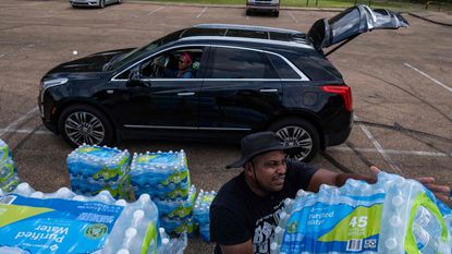 picture of man putting bottled water in another person's car