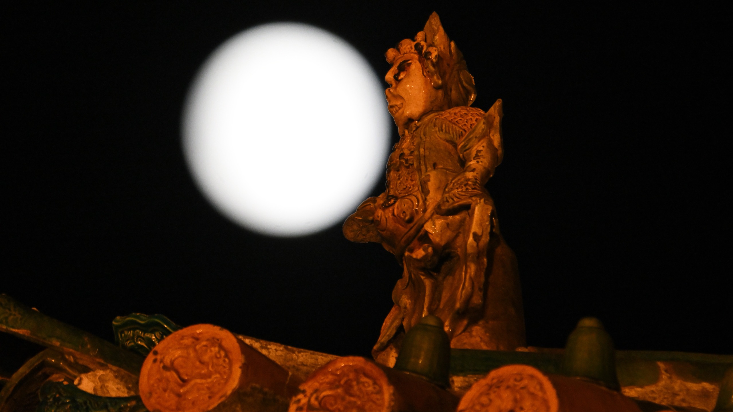 A large full moon rises above the traditional rooftops of the ancient city of Pingyao, China.