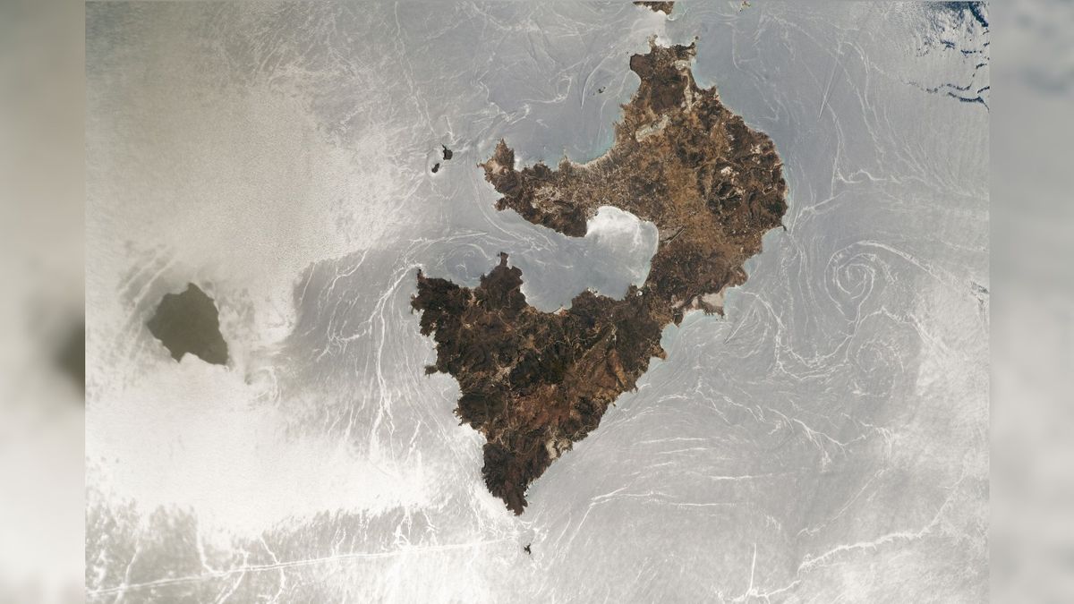 An astronaut photo of two islands with a silver mirror-like ocean surface caused by a sunglint