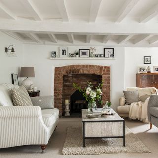 White living room with painted beams, two sofas and brick fireplace