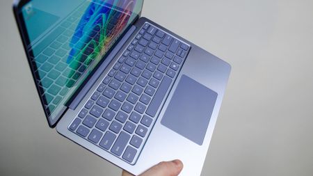 A masculing hand holding the Microsoft Surface Laptop 13-inch at an angle