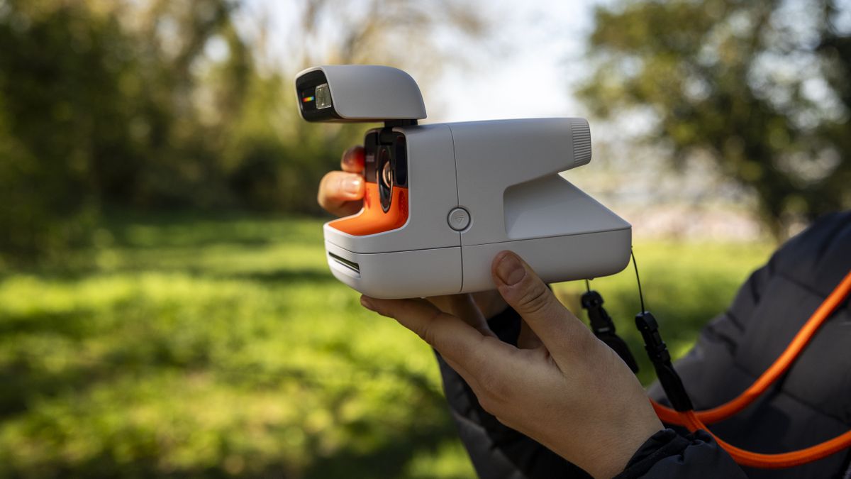 A female photographer holds the Polaroid Flip instant camera in a sunny field