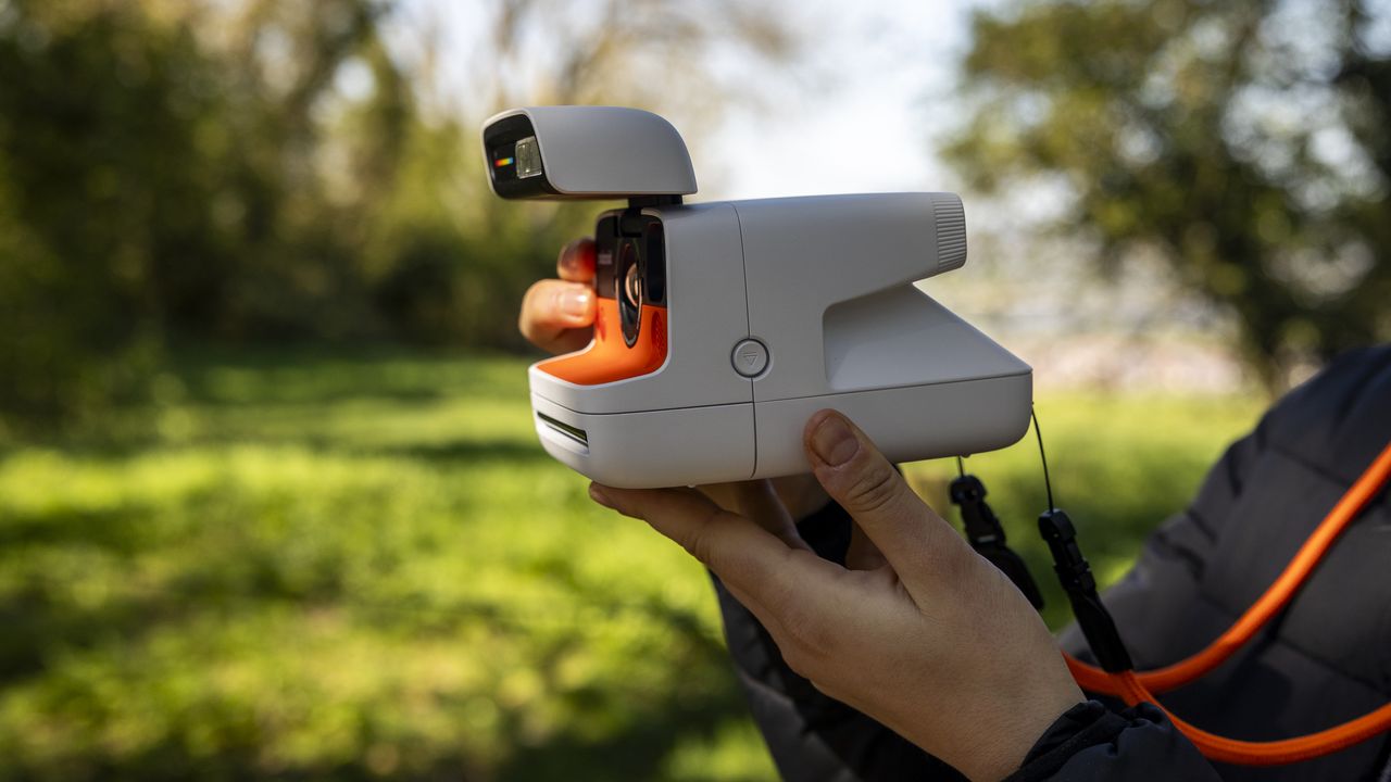A female photographer holds the Polaroid Flip instant camera in a sunny field