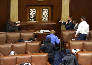Capitol police officers point their guns at a door that was vandalized in the House Chamber.
