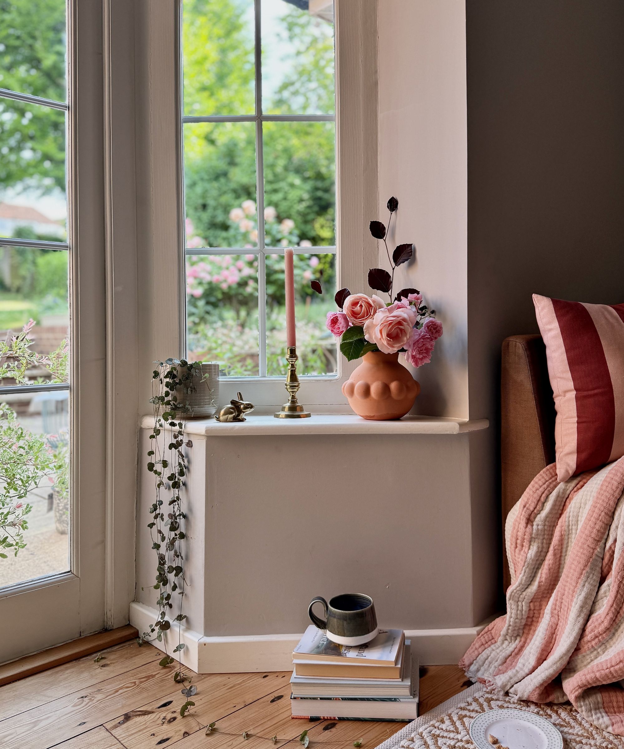 living room corner with creamy beige walls and window shelf decorated with a gold candle holder and terracotta vase with pink roses