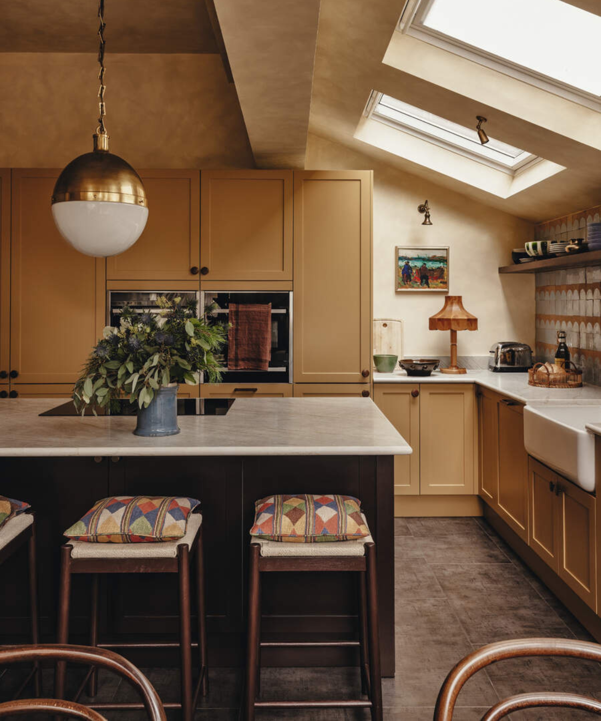 A large country kitchen with ochre cabinets and a maroon island