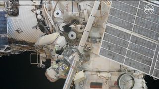 two astronauts in white spacesuits climb on white cylinders floating in space