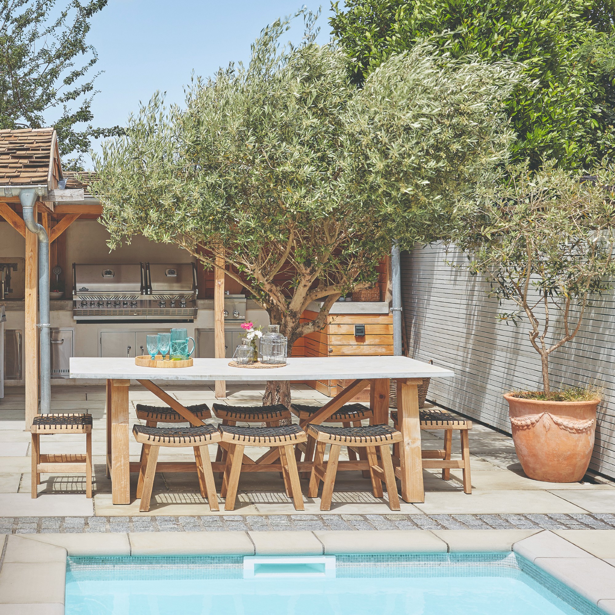 A garden with a pool and an outdoor kitchen with a wooden garden dining set