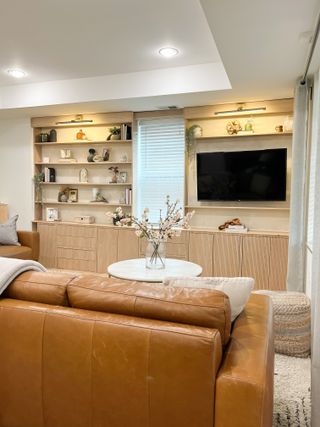 A living room with a brown leather sofa and built-in panelled shelving on one side of the room