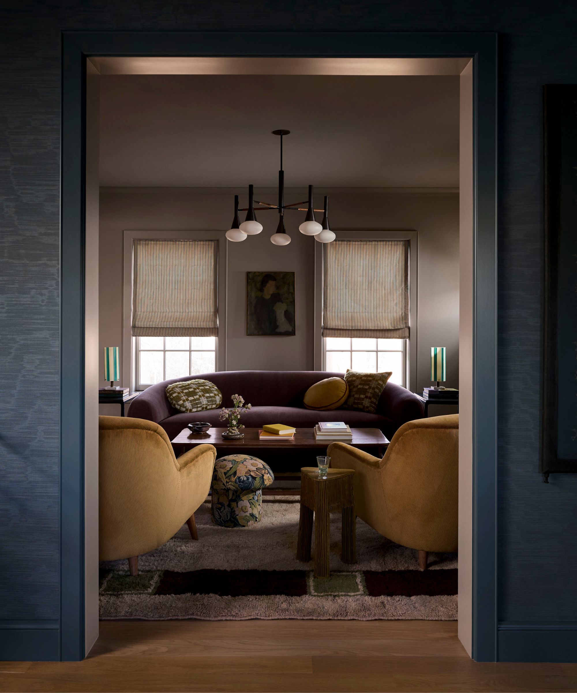 a dark moody living room with a green fireplace, curved dark sofa, two brown armchairs and small floral mushroom stools
