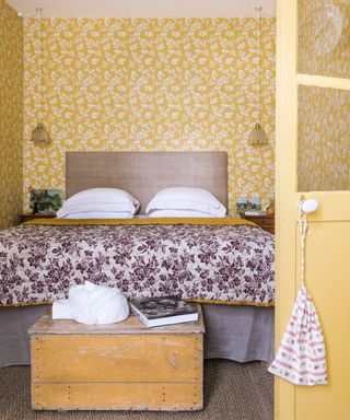 bedroom with yellow floral wallpaper and matching door lilac bedding, vintage chest, pendant lights