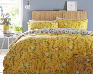 Yellow floral duvet and pillow cover set by French Bedroom Co on a bed with a rattan headboard in a bedroom with grey walls