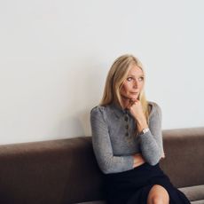 Gwyneth Paltrow sitting on a bench with a ponderous look on her face.