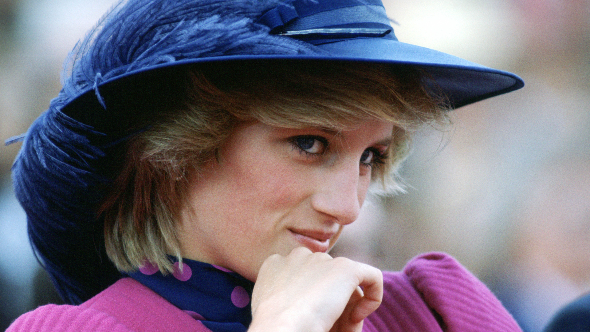 Princess Diana wearing a blue feathered hat and pnik dress leaning her chin on her hand