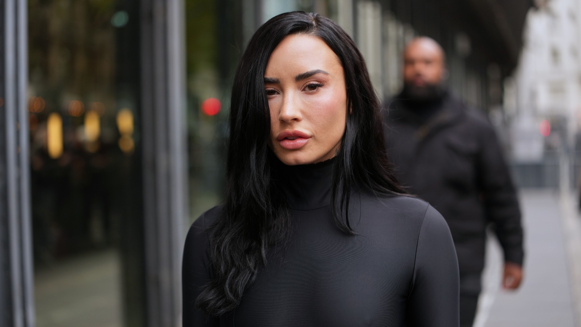 a white woman with long black hair photographed on the street wearing a black turtleneck