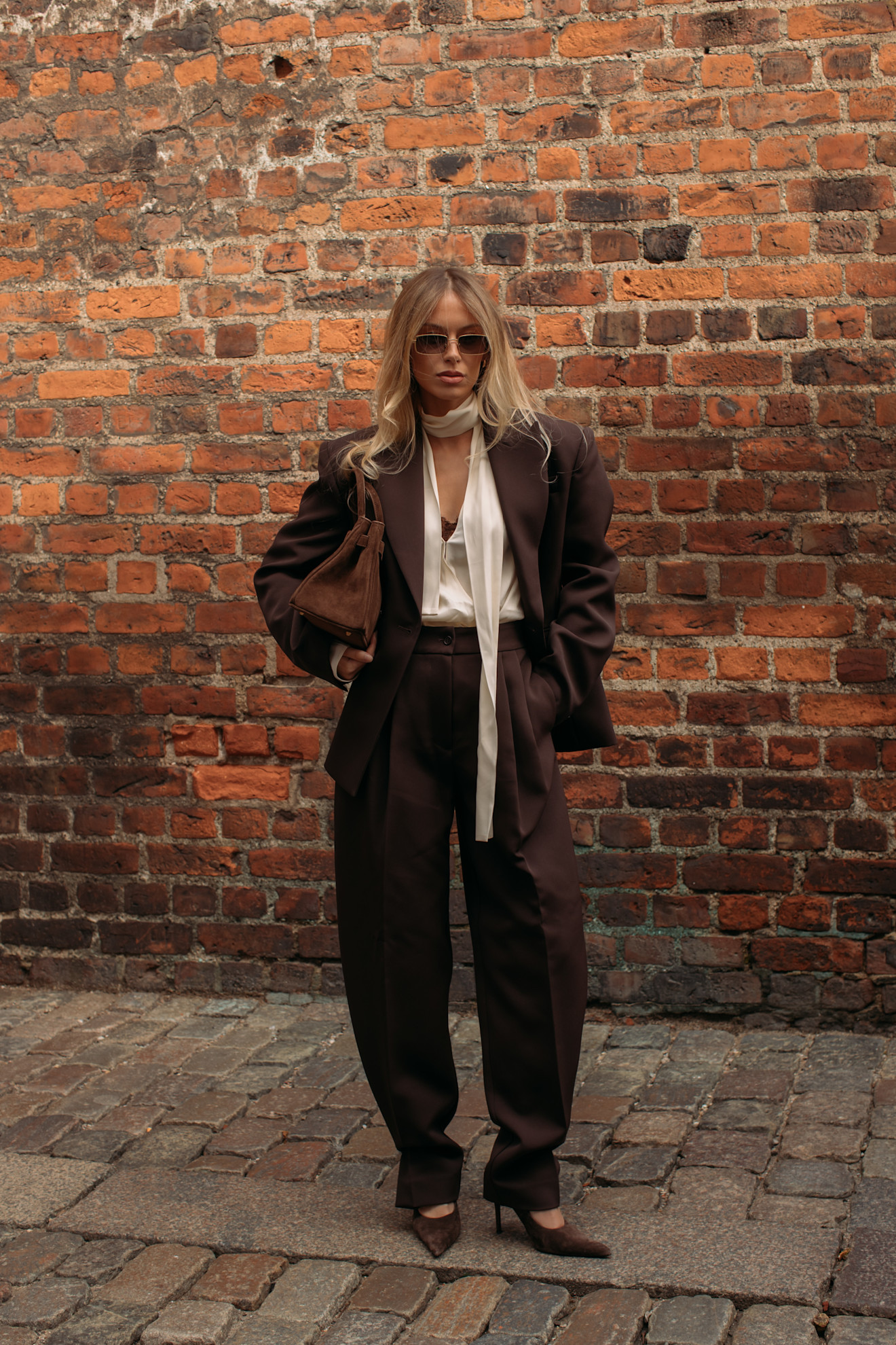 A copenhagen spring 2026 fashion week attendee wears a brown suit and sunglasses in front of brick wall
