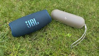 Beats Pill and JBL Charge 5 sitting next to each other on grass