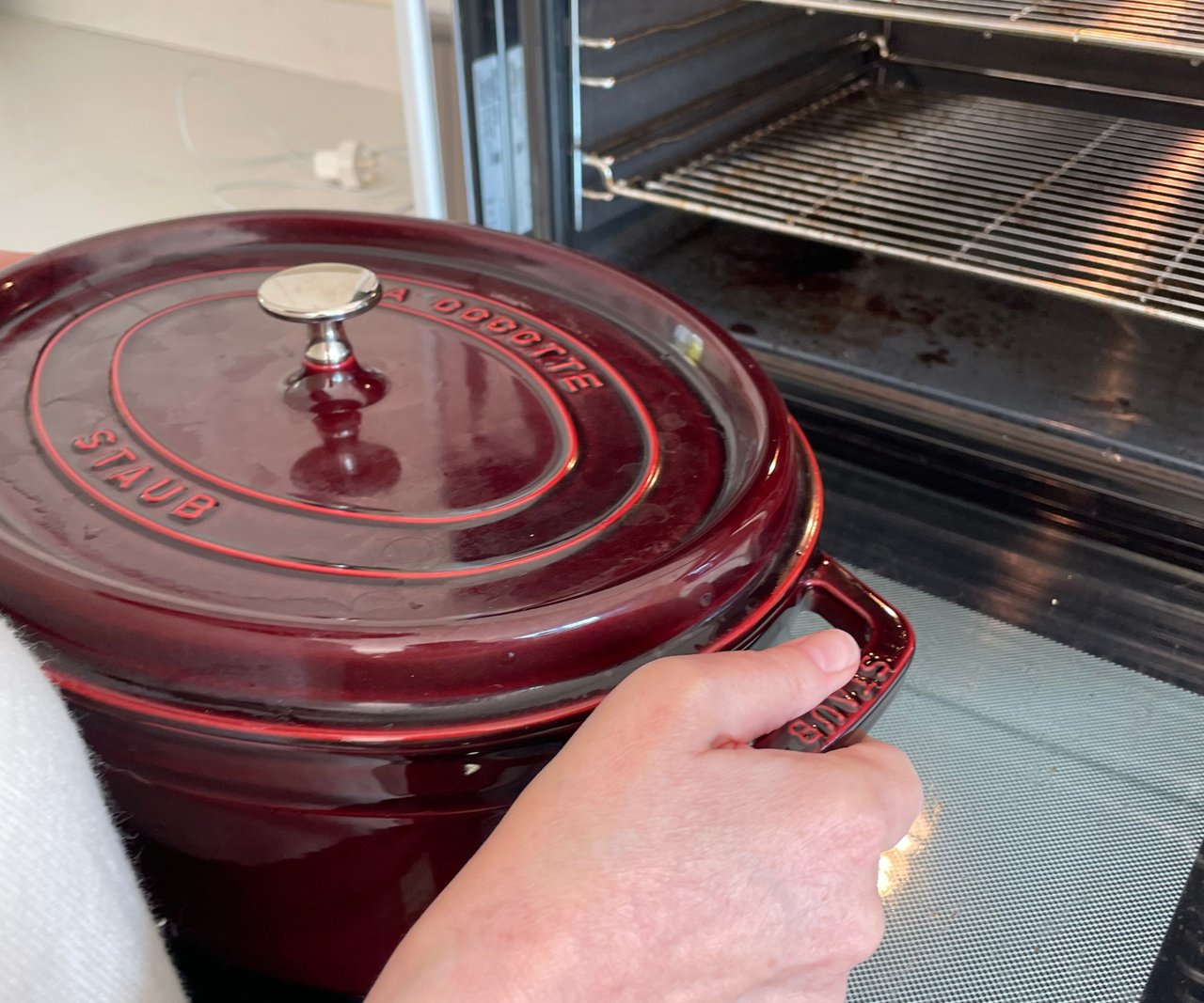 Someone is carrying a deep red colored Dutch oven towards an open oven.