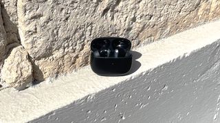 EarFun Air 2 in charging case outdoors by a stone wall