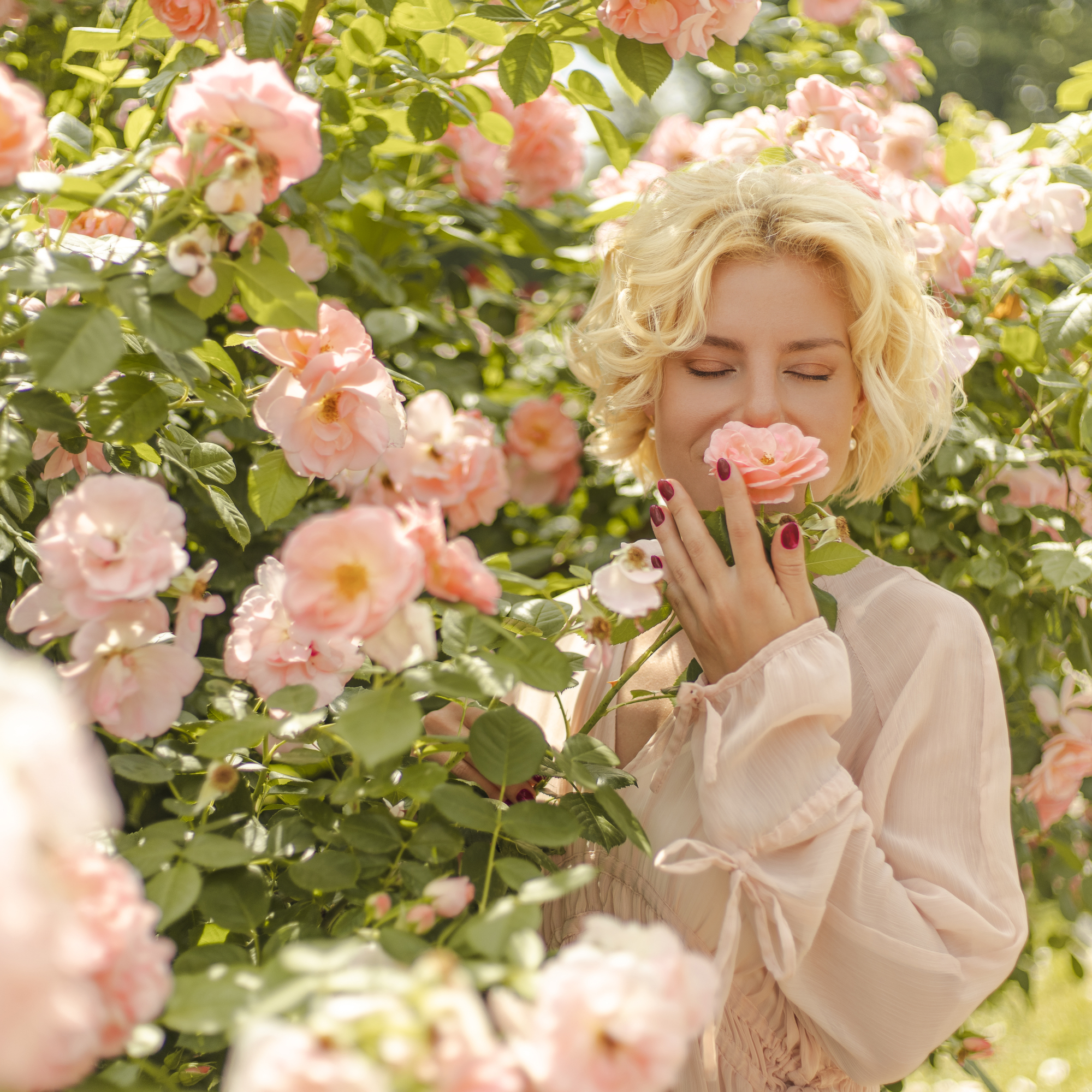 woman smelling a perfect rose with peach-colored petals, inhaling its floral scent