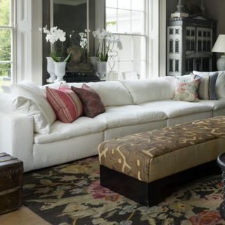 Large white sofa in traditional living room with ottoman and orchids