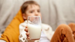 image shows a young boy pushing away a glass of milk